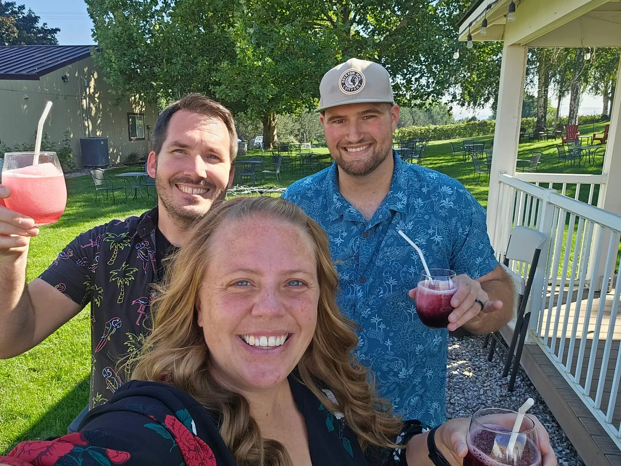 Three of us with frozen drinks in hand, smiling for a selfie on a sunny lawn with tables and trees behind us