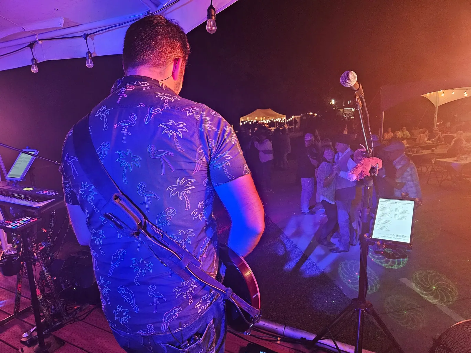 From behind our guitar player on stage, looking out at people dancing under string lights at night.