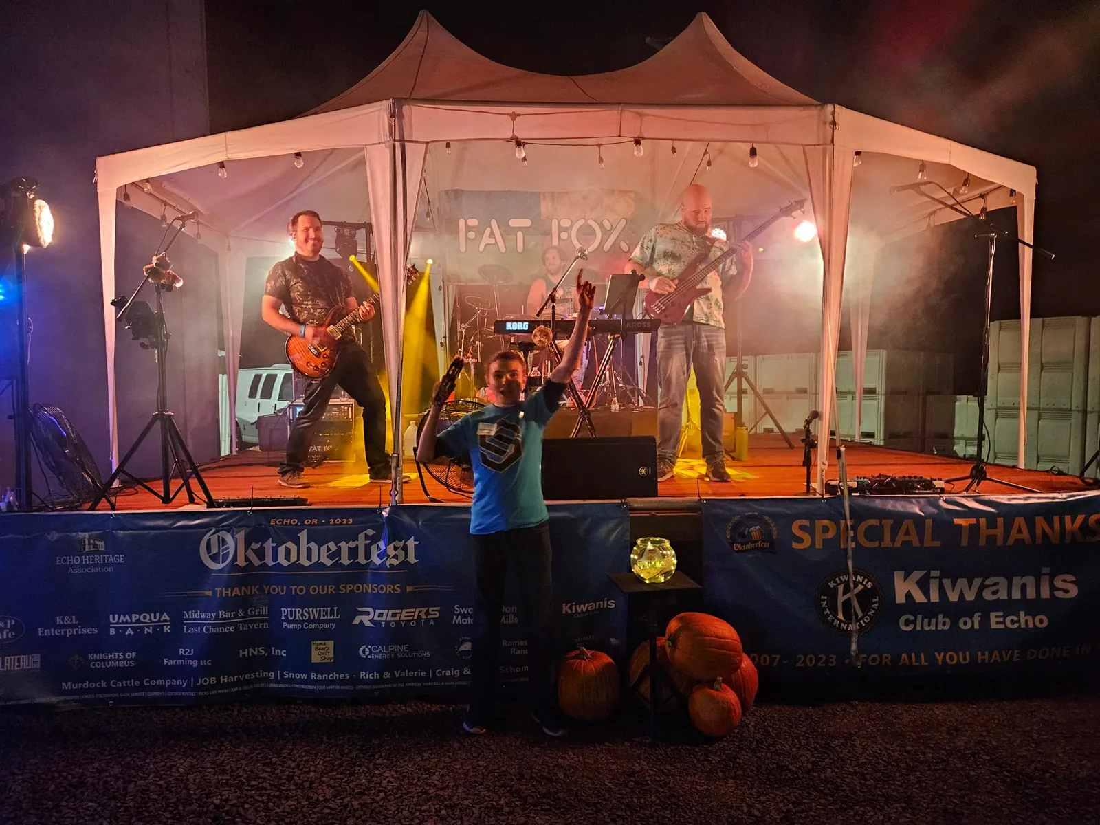 A kid throwing an arm up in front of the stage as we play under our Fat Fox banner at Oktoberfest 2023 in Echo, OR.