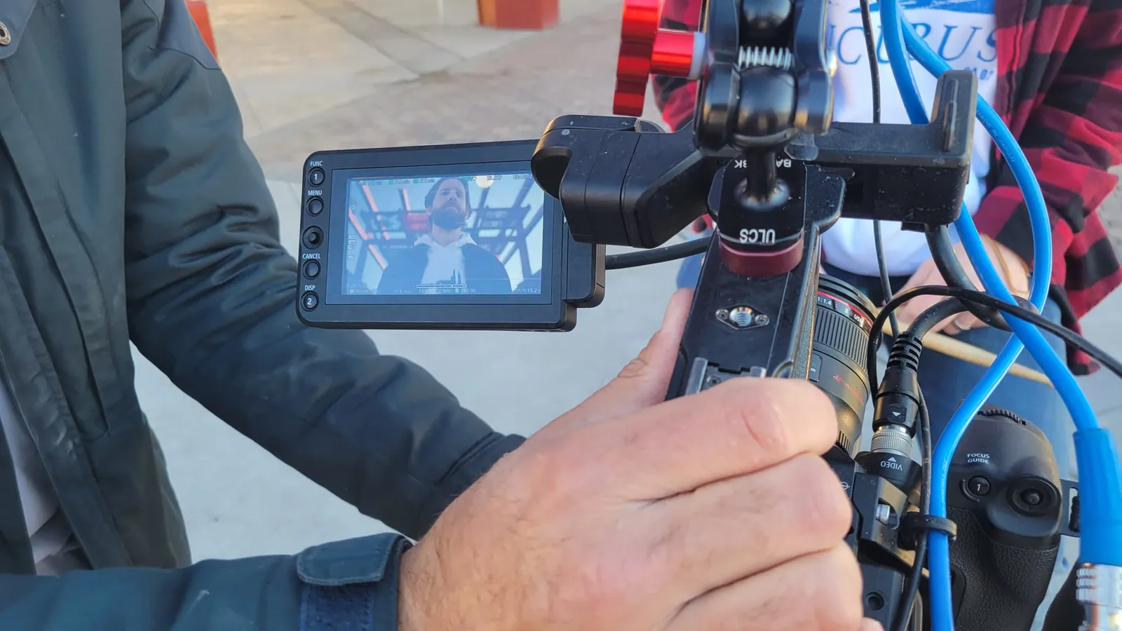 A camera operator's hands on the rig, its flip-out screen framing one of us during the video shoot.
