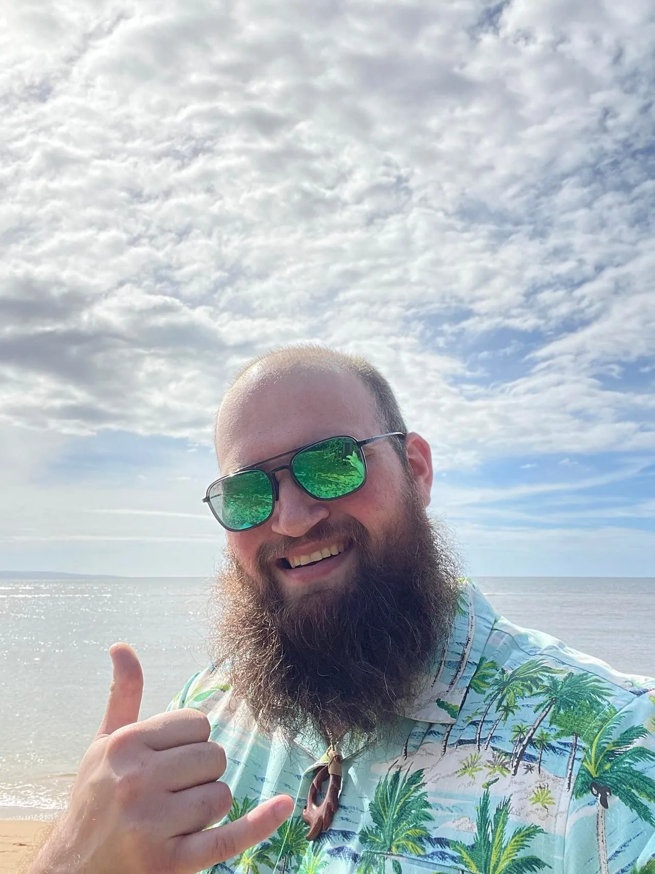 Brian flashing a hang-loose sign on the beach in a Hawaiian shirt and green mirrored sunglasses.