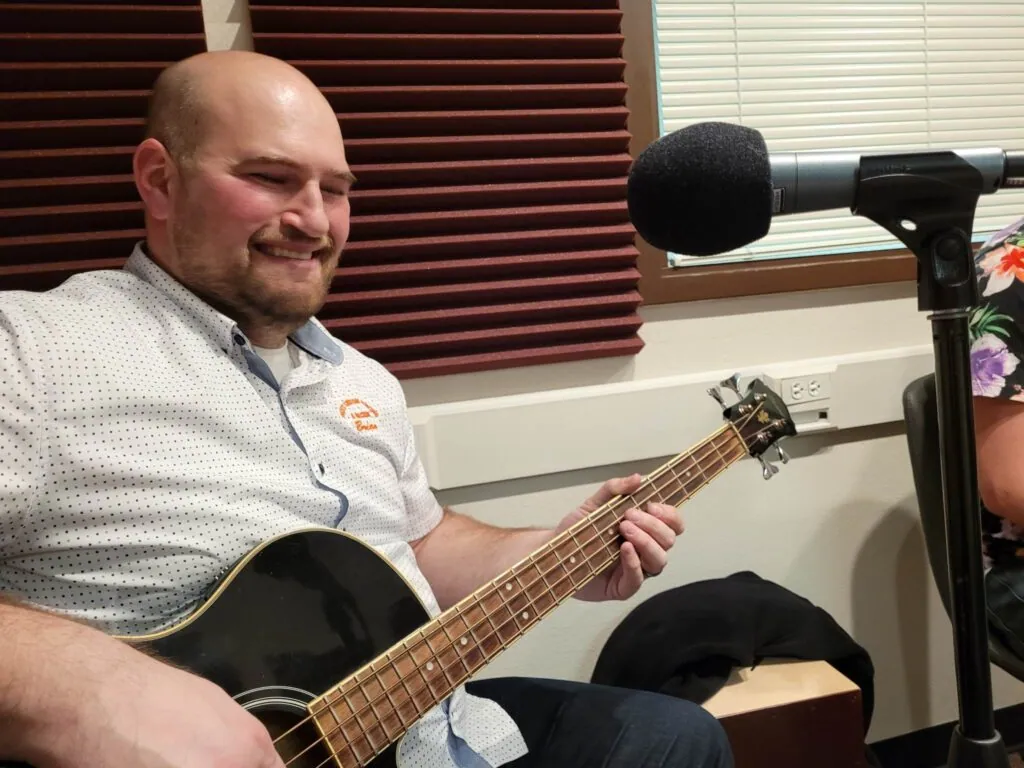 Our bass player smiling as he plays an acoustic bass in front of a mic in the studio.