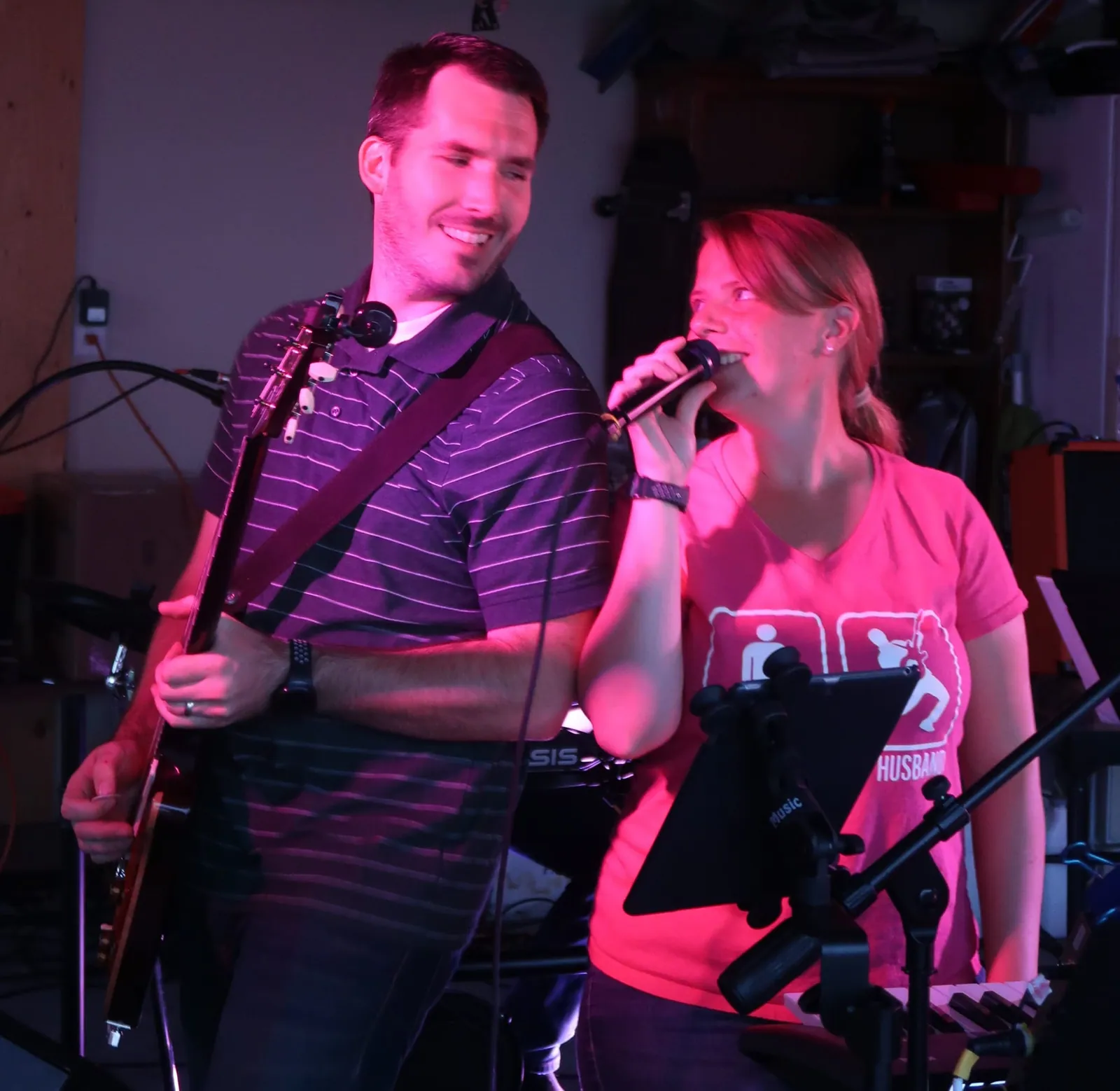 Kali singing and Tommy playing guitar side by side, sharing a smile under pink stage lights.