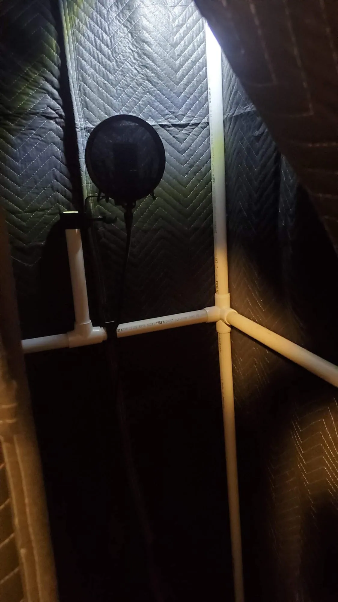 Inside the booth: a mic behind a round pop filter, walled in by quilted blankets on the PVC frame.