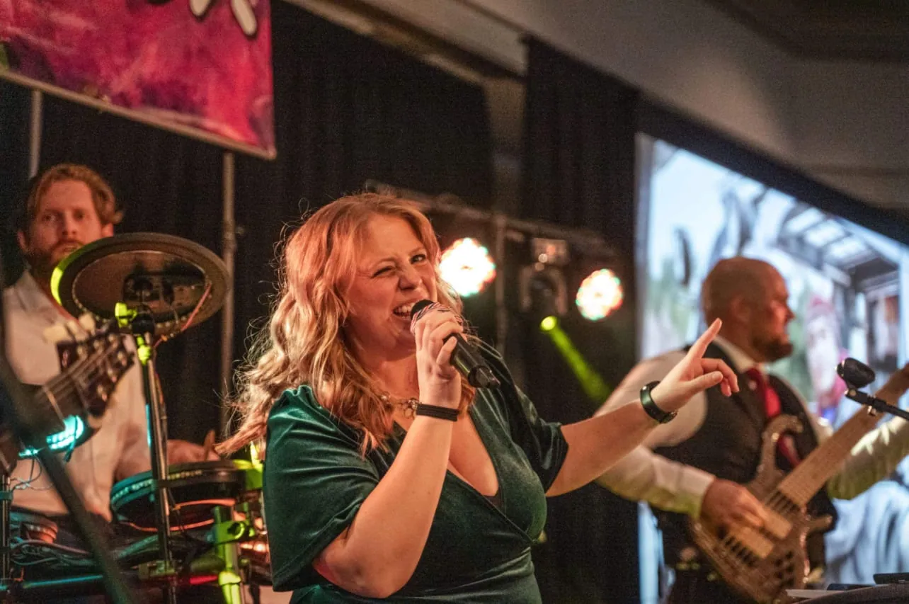 Our singer in a green velvet dress singing and pointing, with drums and bass playing behind her under stage lights.
