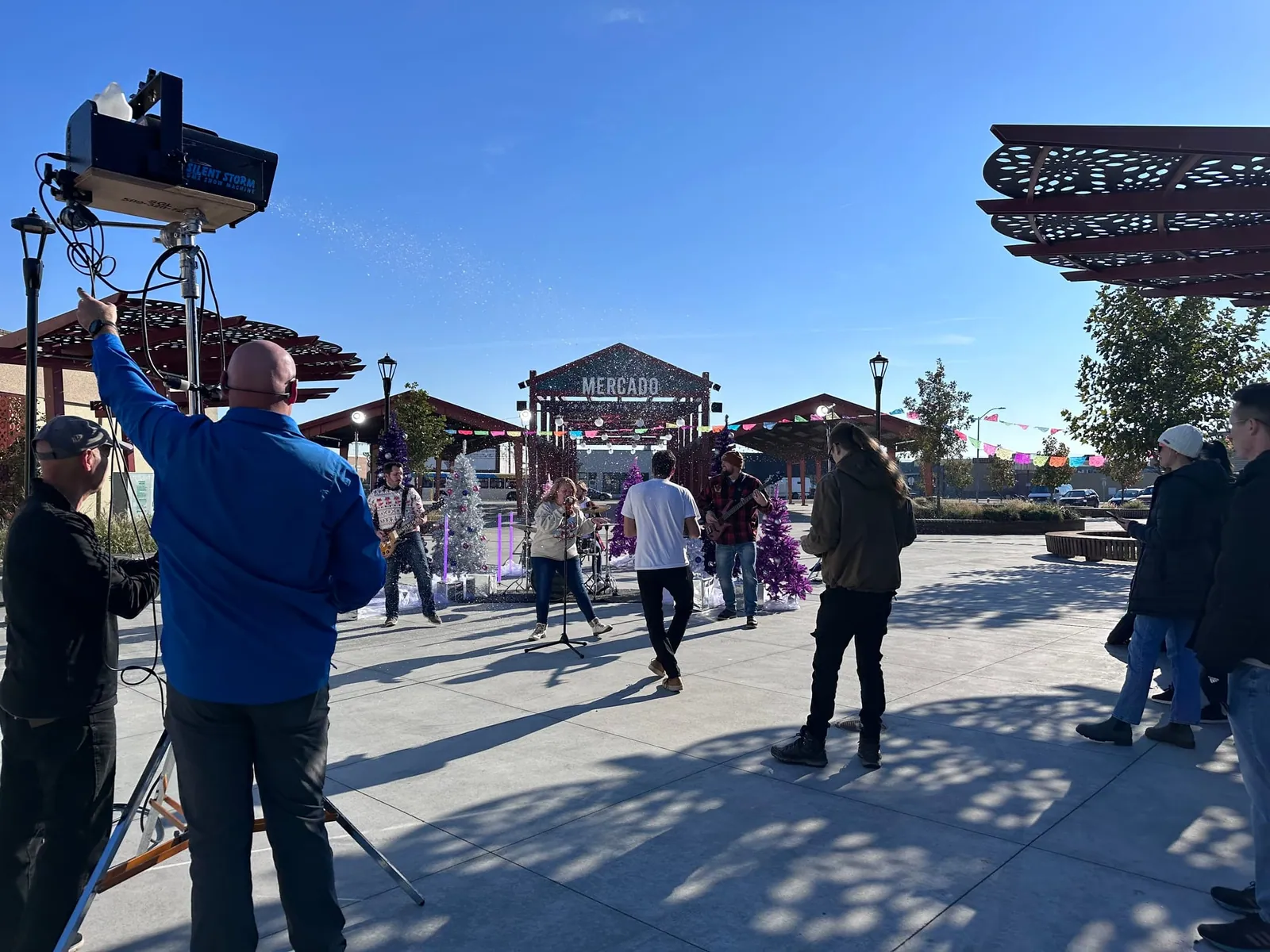 A crew member works the snow machine as we play among purple Christmas trees in front of the Mercado sign at Peanuts Park.