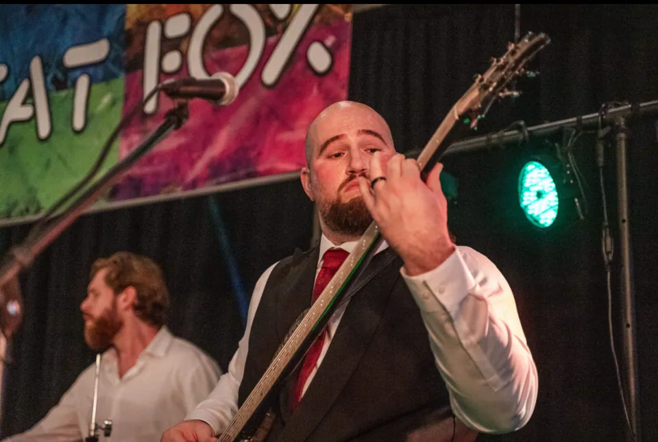 Our bass player, in a vest and red tie, playing in front of our Fat Fox banner