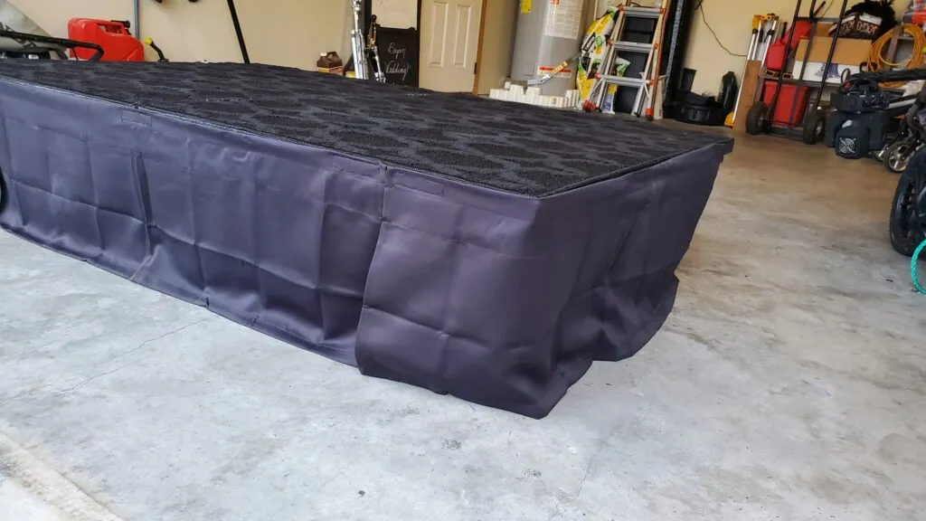 A carpeted stage riser in the garage, its sides wrapped in a dark fabric skirt.