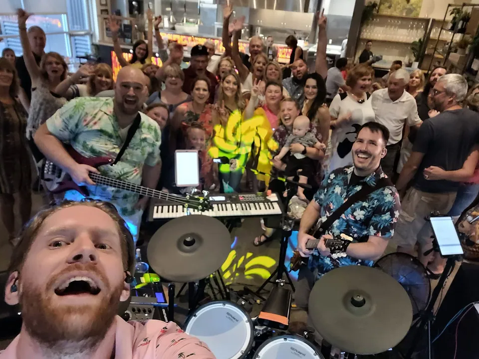 Our drummer's selfie from behind his kit: our bass player and guitarist grinning, a crowd behind them cheering with their hands in the air
