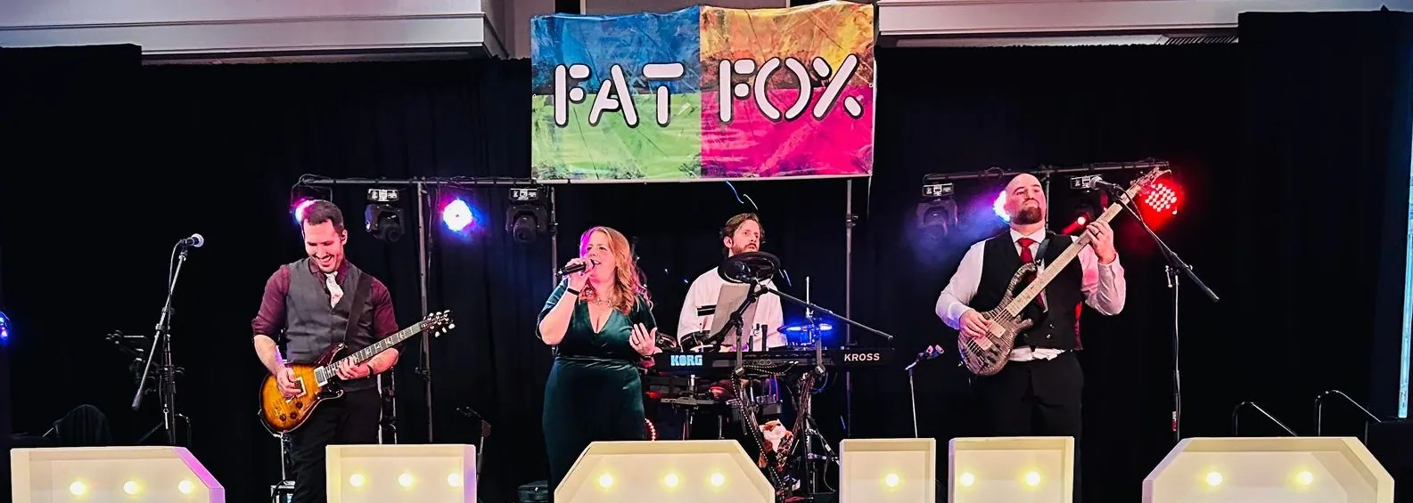 The four of us playing on a ballroom stage under our Fat Fox banner, lights glowing along the front of the stage