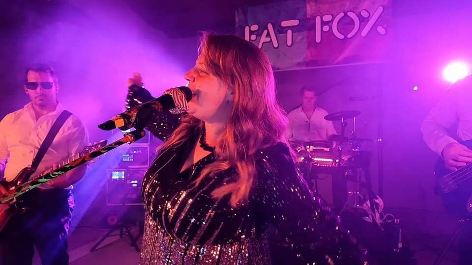 Our singer belting out a song under pink and purple stage lights, the band behind her