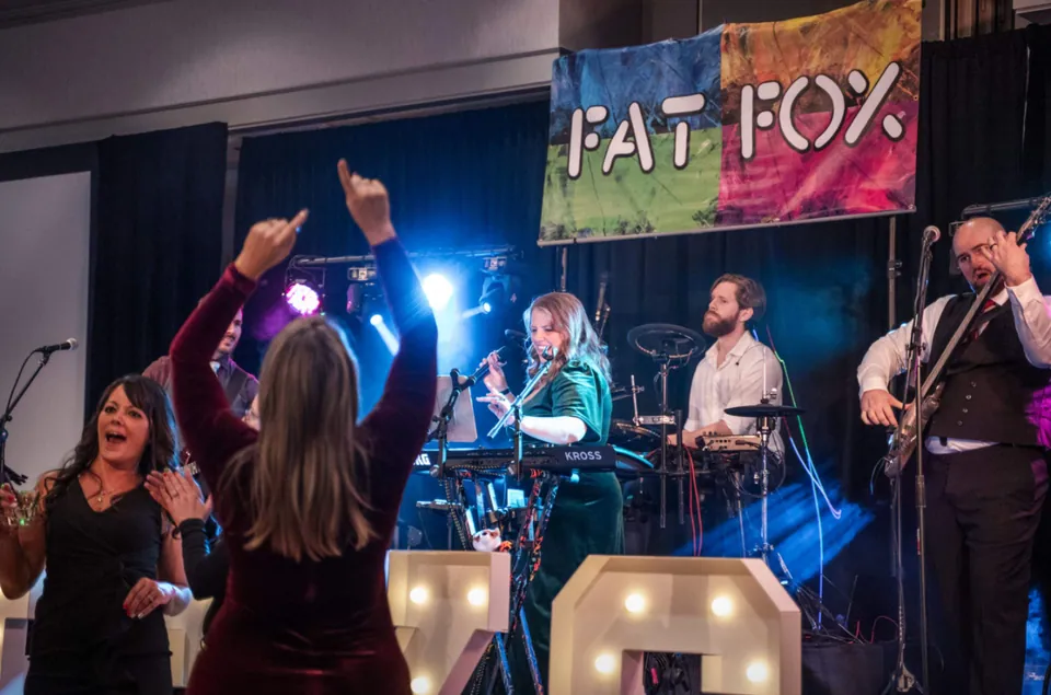 Two guests dancing in front of the stage, one with both arms in the air, while our singer sings at her keyboard