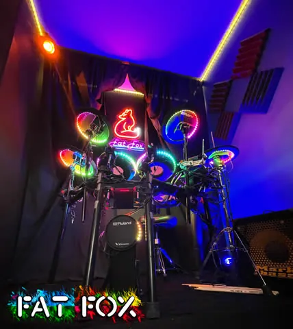 Our revamped studio room: a Roland electronic drum kit lit up with rainbow LED rings, a neon Fat Fox sign, and colored lights along the ceiling