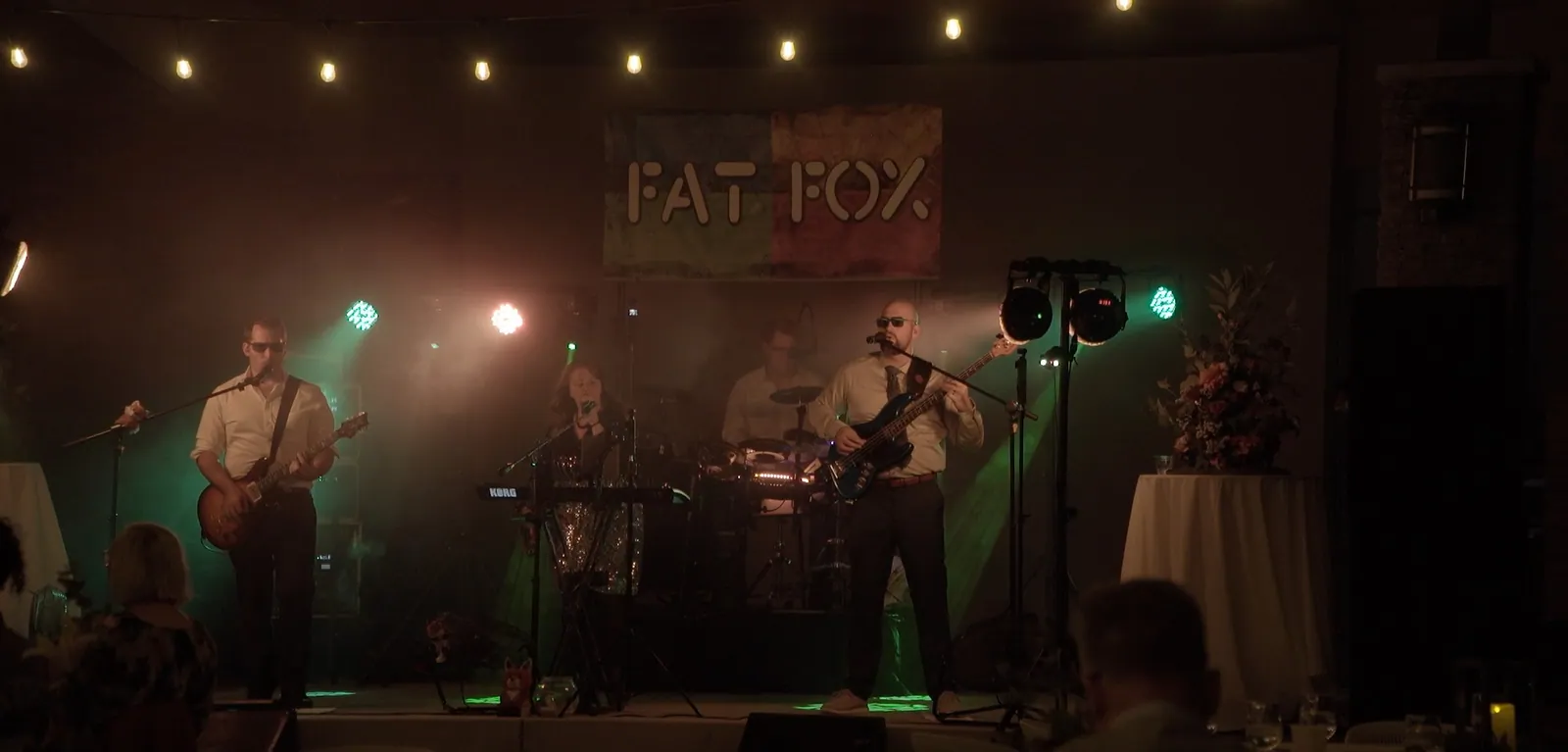 Our band playing on a stage under string lights and our Fat Fox banner, guests watching in the foreground