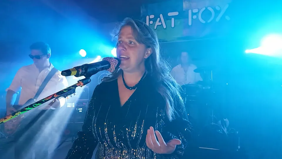 Our singer singing in a sparkling dress under blue stage lights, the band behind her